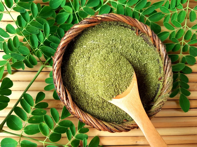 Moringa powder on a bamboo mat with a wooden spoon